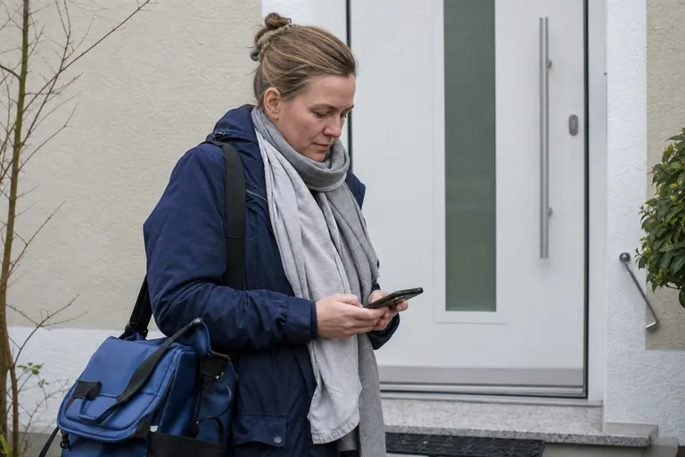 Hebamme dokumentiert einen Hausbesuch auf einem Smartphone vor einem Wohnhaus